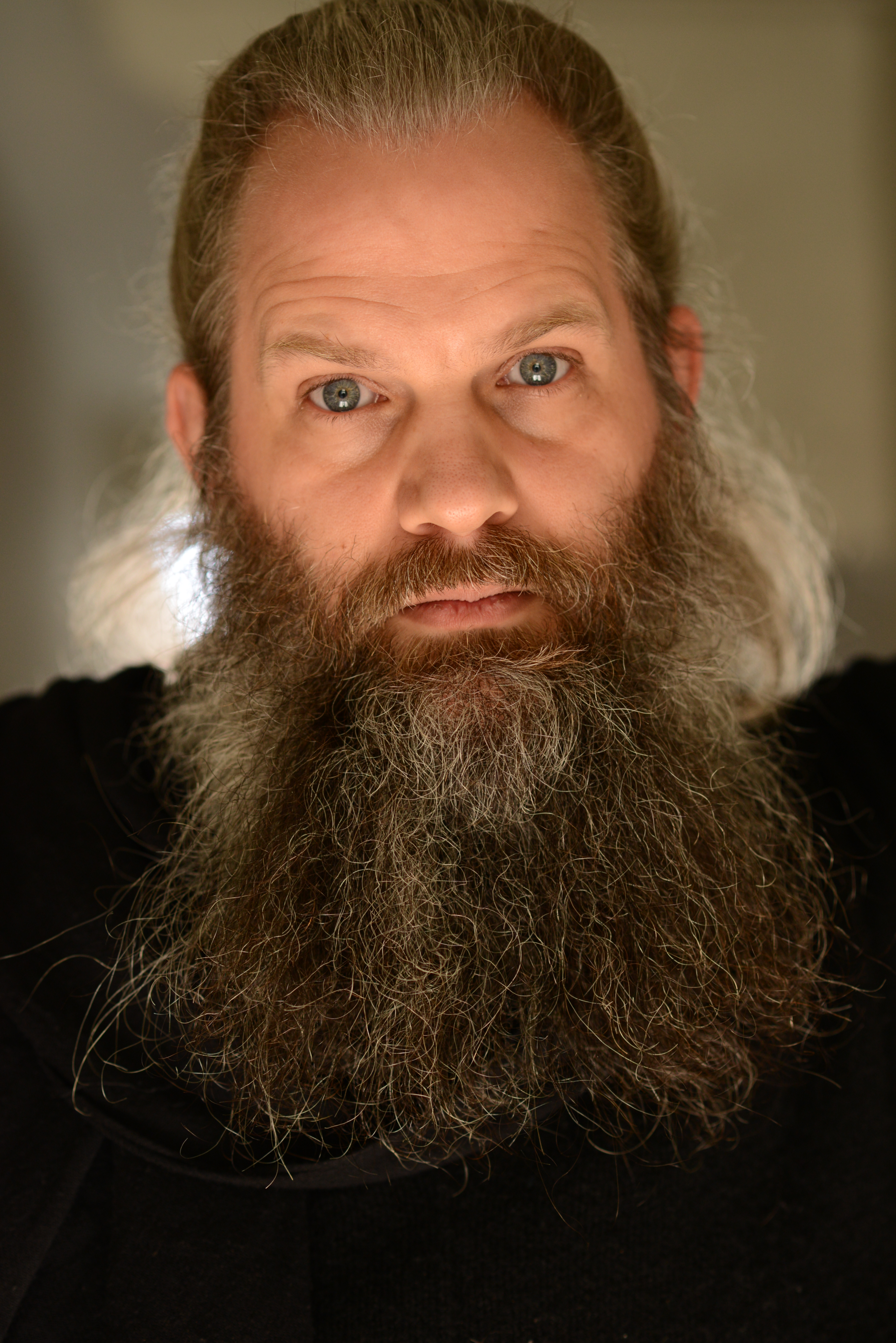 Bearded Man with hair pulled back, wearing black, looking either like an artist who takes himself too seriously or like a villain maybe both